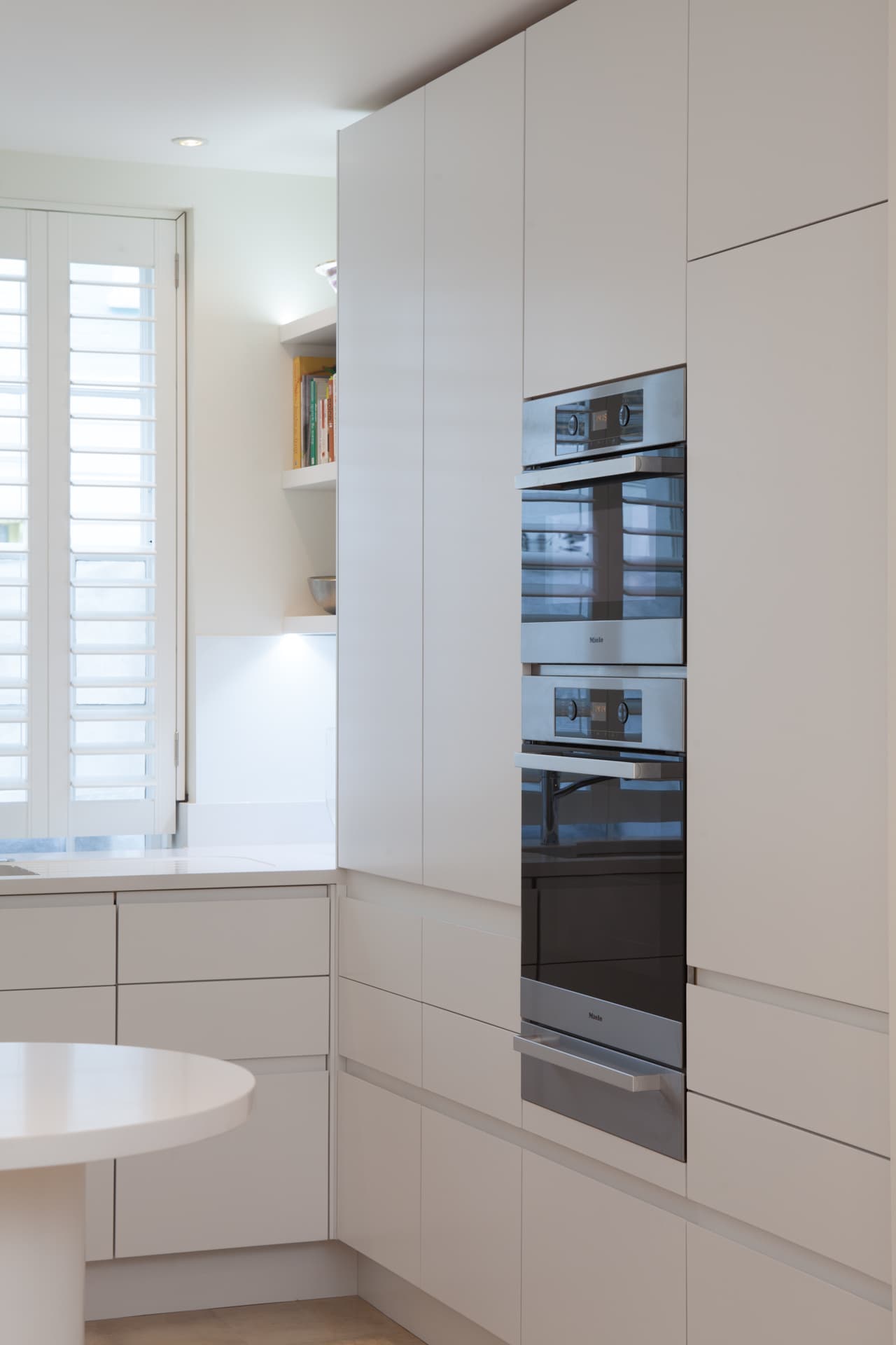 Modern white kitchen with integrated Miele ovens and shutters