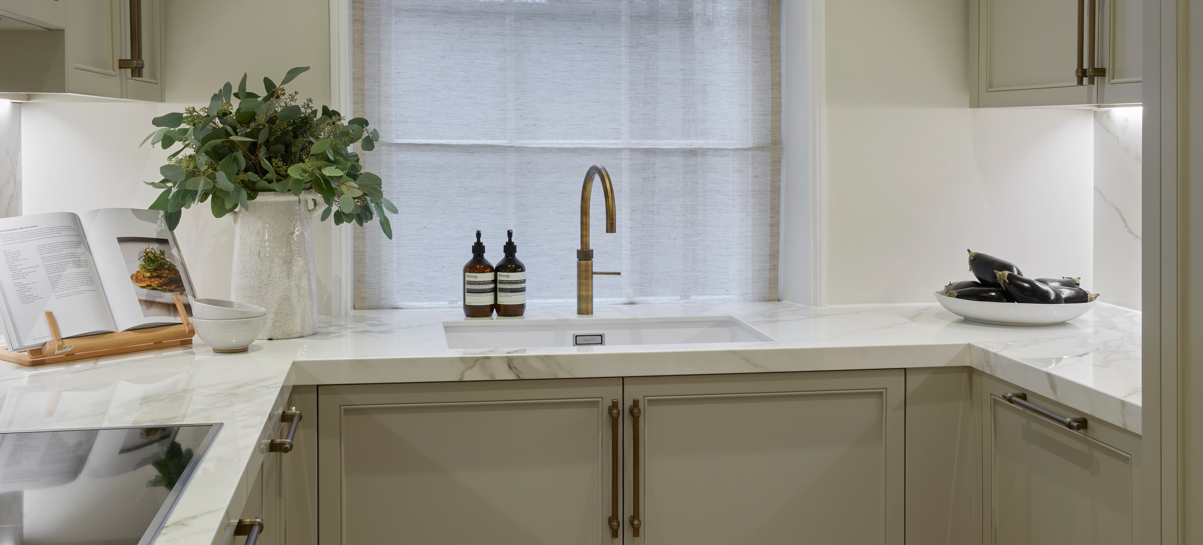 Sage green cabinetry with marble worktop and brass tap